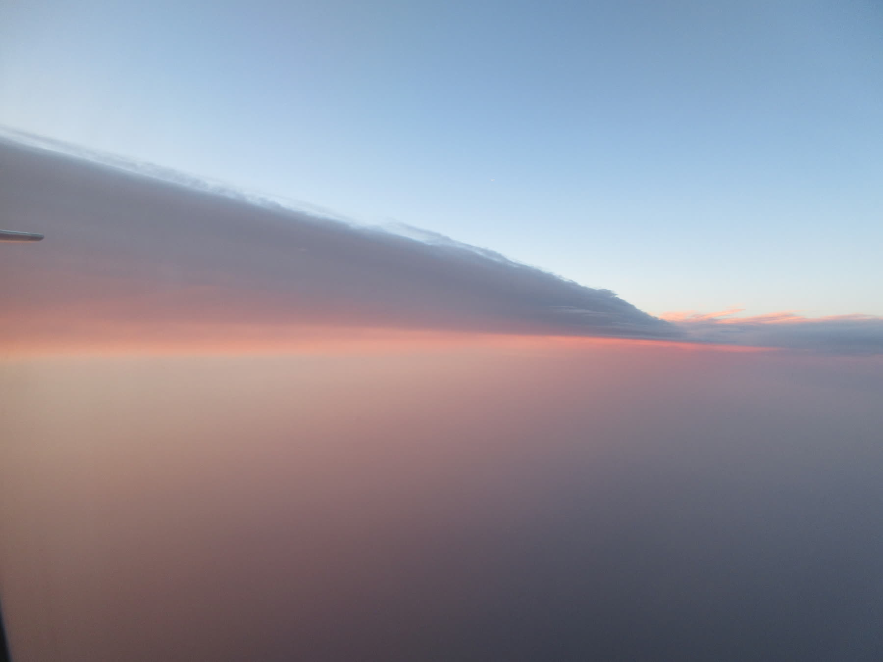 A pastel horizon and long cloud bank viewed from an airplane window.