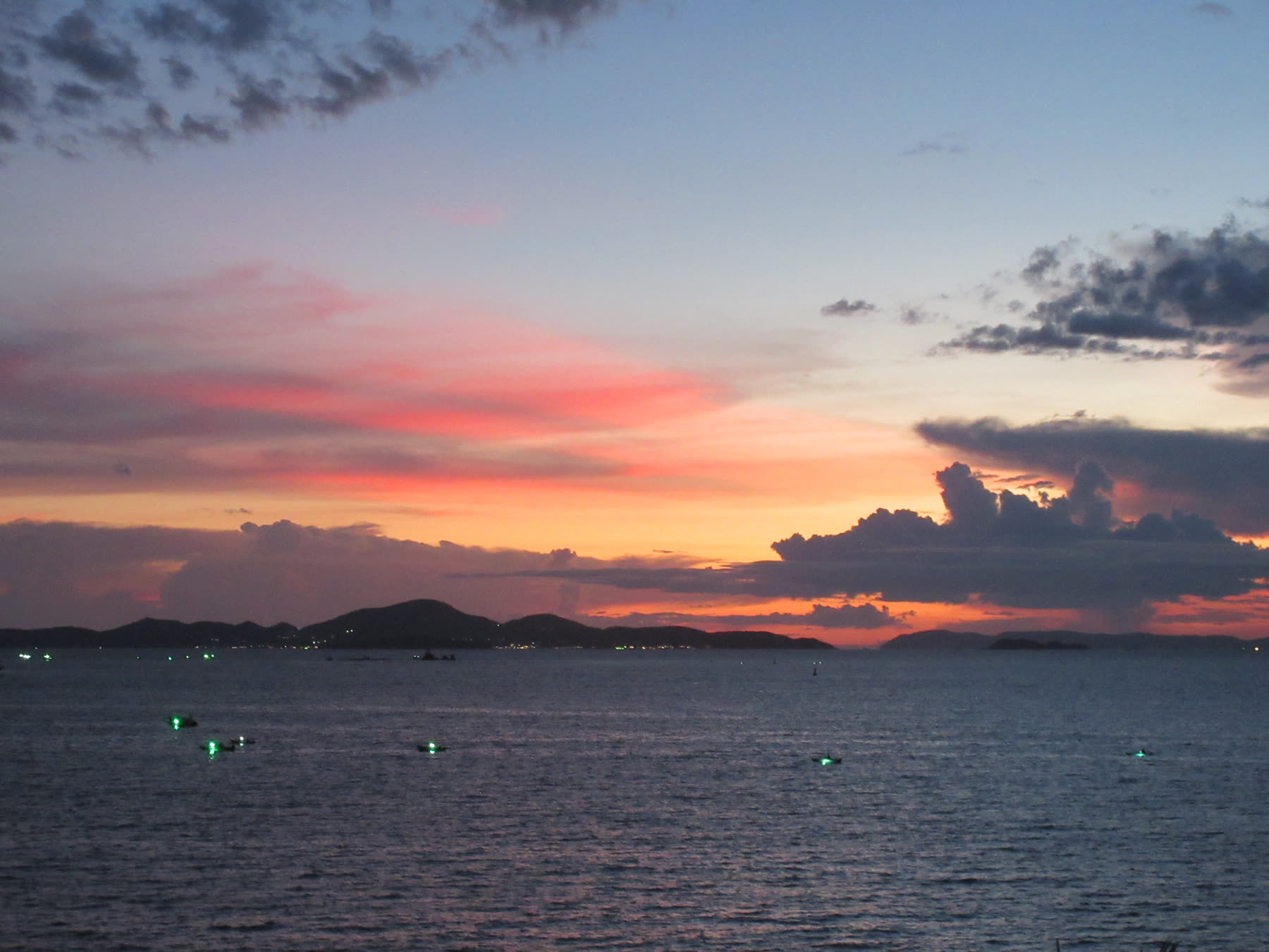 A vivid sunset over the sea with dark clouds and island silhouettes.