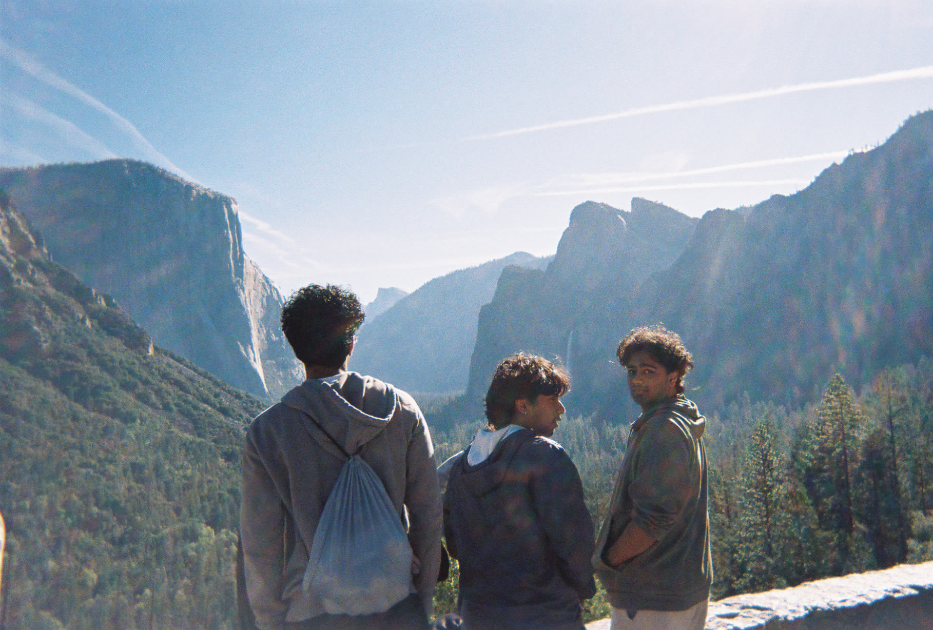 Three friends standing at an overlook with a wide mountain valley behind them.