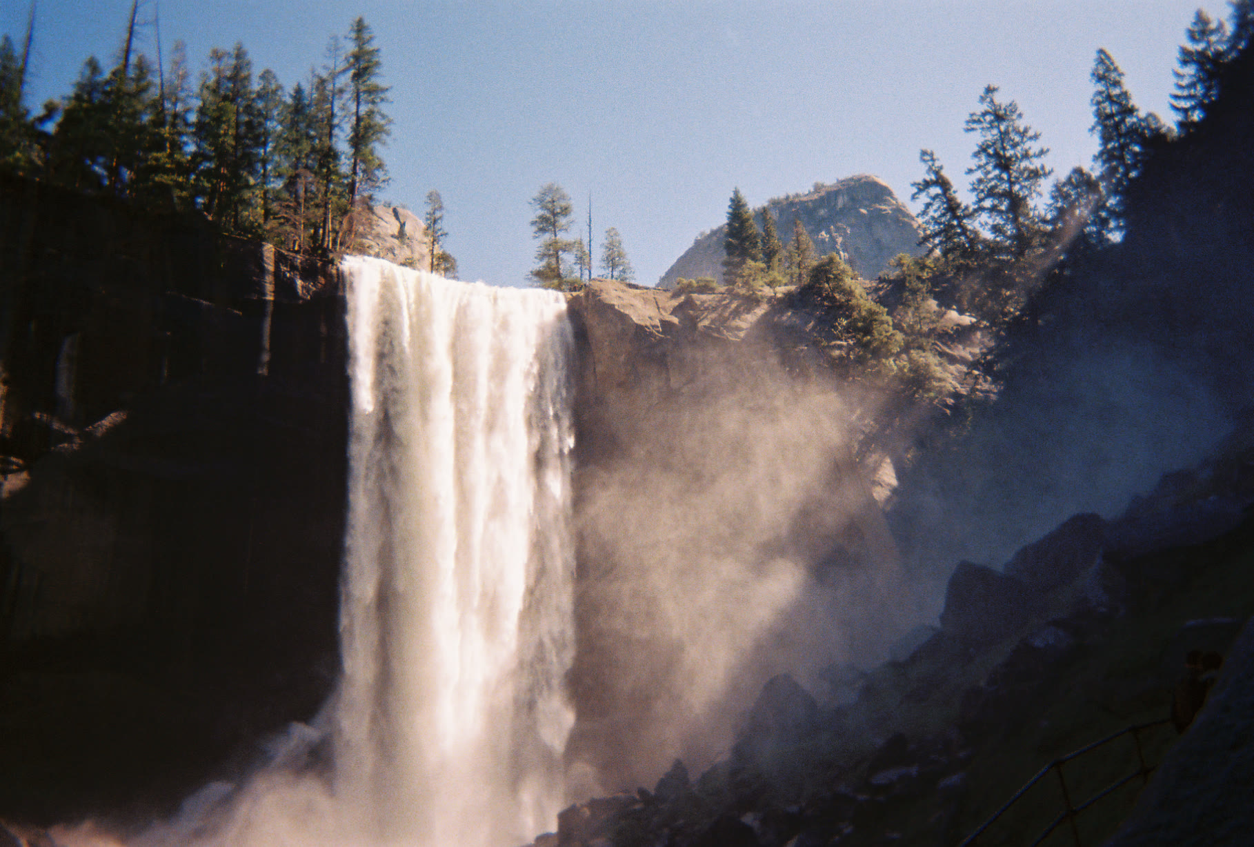 Film photograph of a waterfall lit by the sun with mist rising beside it.