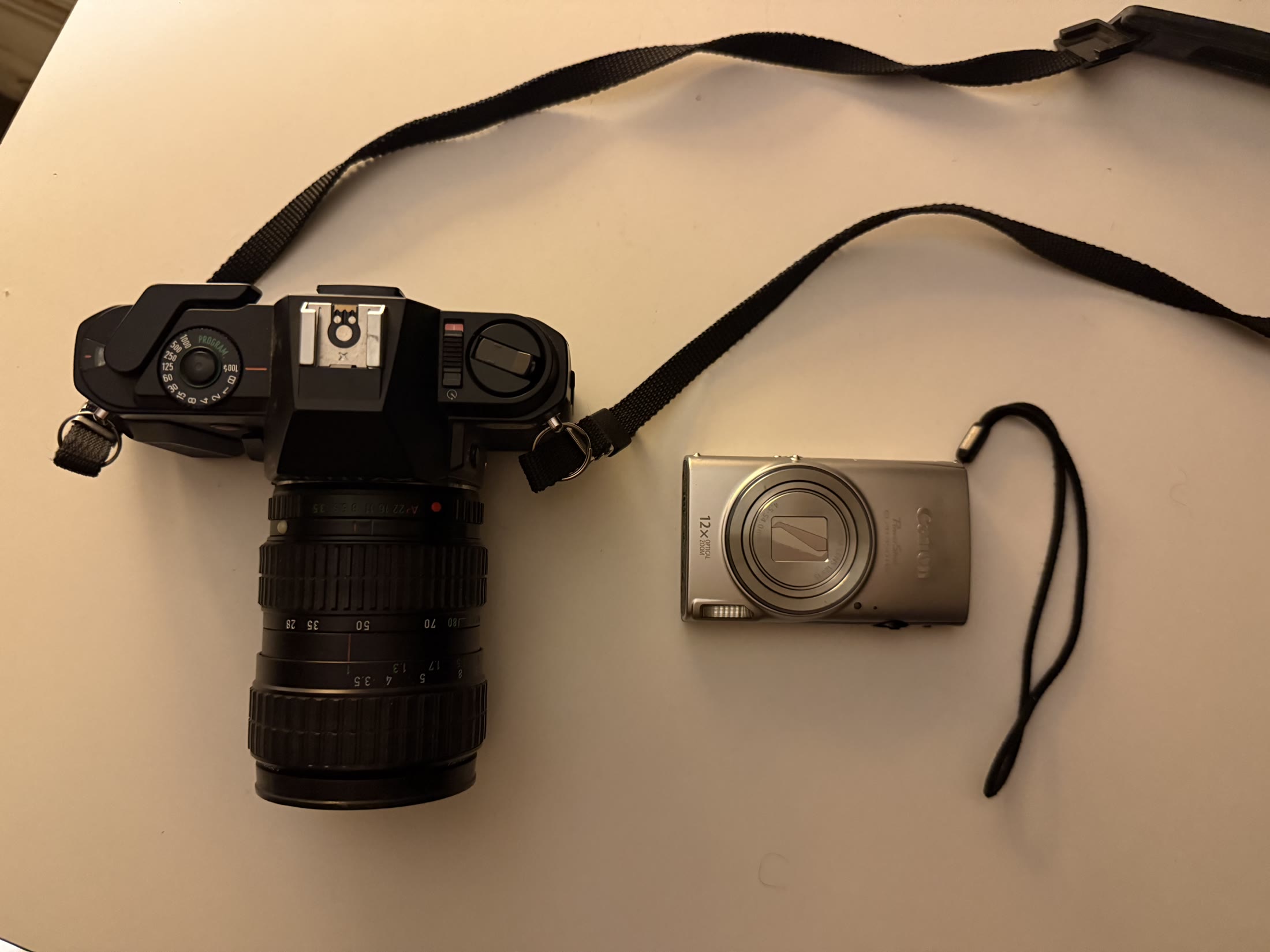 The black Pentax P3 film camera beside a small silver Canon point-and-shoot camera.